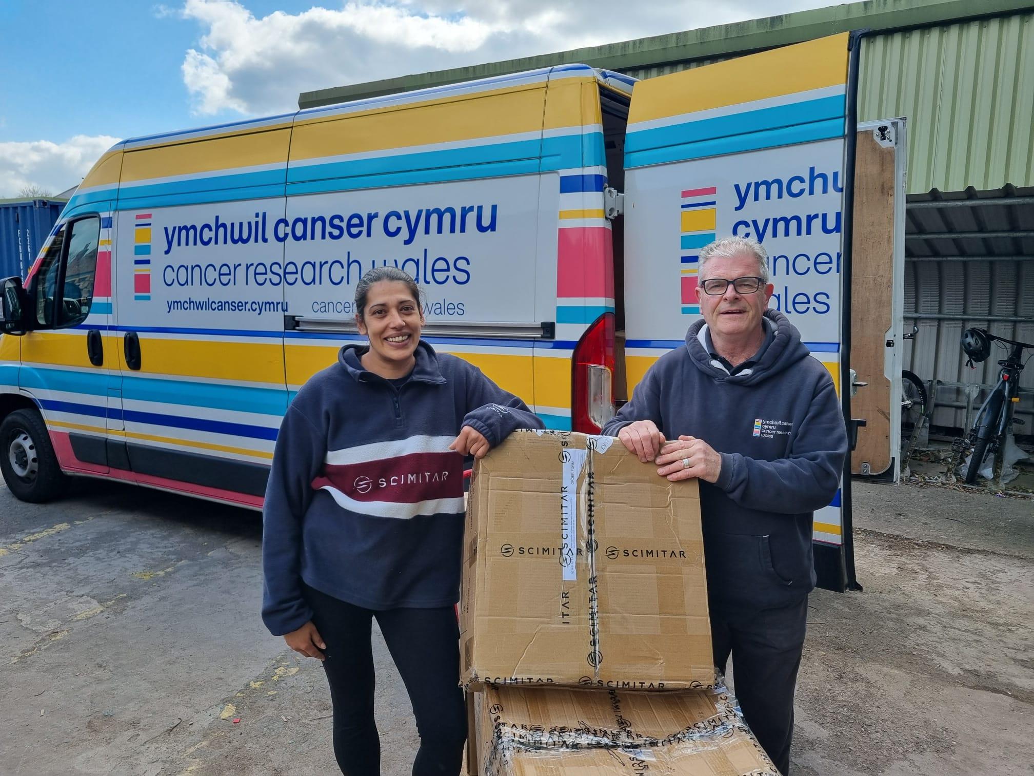 Scimitar Sports staff delivering branded merchandise boxes to a Cancer Research Wales van