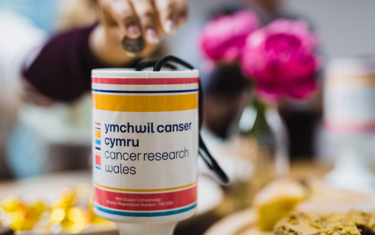 Person donating coins into a Cancer Research Wales collection tin